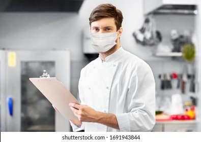 Cooking, Profession And People Concept - Male Chef Cook With Clipboard Wearing Face Protective Medical Mask Over Restaurant Kitchen Background