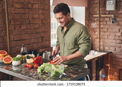 Cooking In Quarantine. Smiling Attractive Cheerful Man Cutting A Bell Pepper With A Chefs Knife