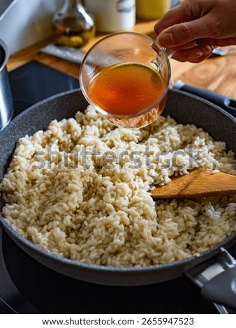 Cooking risotto in frying pan. Adding broth to risotto