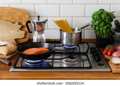 Cooking Salmon Fillet And Spaghetti On A Gas Stove In Traditional Home Kitchen. Wood Worktop.