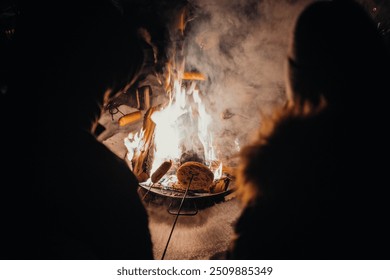 Cooking sausages over fire in snow on frozen lake at night near Rovaniemi, Lapland, Finland - Powered by Shutterstock