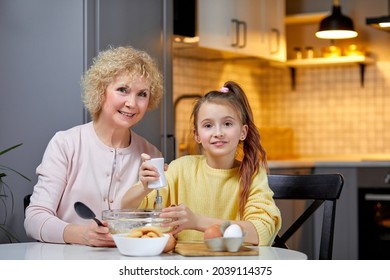 Cooking With Soul. Happy Little Girl Help Senior Grandma At Kitchen Mix Dough For Cookies Pancakes.Portrait Of Older Granny Teach Small Grandkid To Bake Homemade Cake Pastry Share Family Recipe