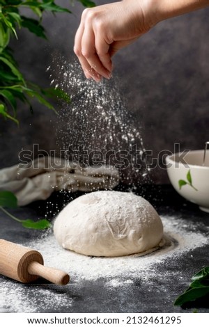 Cooking sourdough homemade bread. Sieving flour over raw bread dough on table, dark background, selective focus.