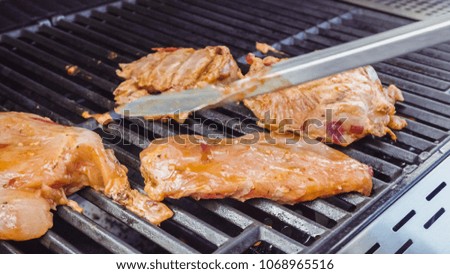 Cooking spicy chicken breasts on gas grill outdoors.