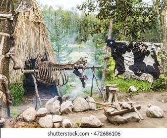 Cooking Stone Age Human Food On The Hearth On Fire In Front Of The Hut. Dried Cow Hide. Wood Carved With Symbols And Bones. Parking Ancient Man