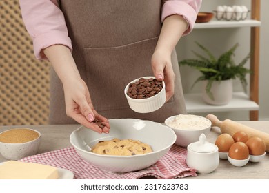 Cooking sweet cookies. Woman adding chocolate chips to dough at table in kitchen, closeup - Powered by Shutterstock