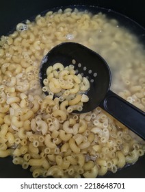 Cooking Tasty Macaroni Pasta Into Boiling Water In A Pot Saucepan On Stove With Spatula In The Kitchen. Macaroni In Boiling Water For Making Italian Pasta.