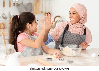 Cooking Team. Cheerful Islamic Mom And Daughter Giving High Five While Baking In Kitchen, Joyful Arab Woman In Hijab And Her Cute Little Female Child Having Fun Together While Making Food At Home