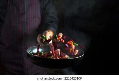 Cooking vegetables in a pan in a chef hand on a black background with copy space. Nutrition concept. Vegetable menu for the hotel - Shutterstock ID 2213423109