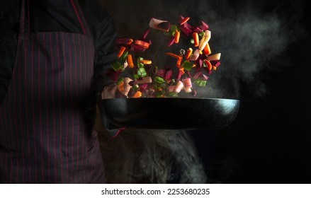 Cooking vegetarian food in a hot pan with steam in the hands of a chef. Place for recipe or menu on dark background - Shutterstock ID 2253680235