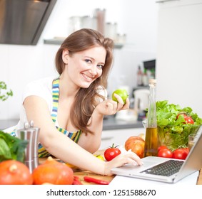 Cooking woman looking at computer while preparing food in kitchen - Shutterstock ID 1251588670