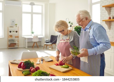 Cooking With Your Sweetheart. Happy Mature Couple Making Healthy Lunch Together In The Kitchen Of Modern Studio Apartment. Smiling Senior Husband Helping His Wife Who's Chopping Vegetables For Salad