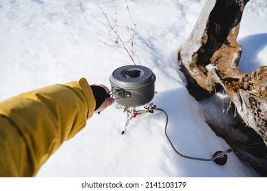 Cooks food on a hike on a gas burner. Camping gas, cooking, hand holding a pot of food, light equipment of a tourist in a winter hike. High quality photo