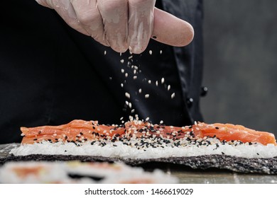 Cook's hands close-up. A male chef makes sushi and rolls from rice, red fish and avocado. White gloves. Dark background.