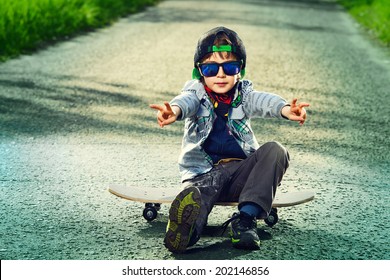 Cool 7 year old boy with his skateboard on the street. Childhood. Summertime.