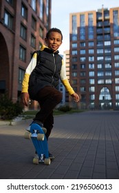 Cool African American Boy Kid Doing Tricks On His Blue Longboard On Cityscape With Multi-storey Building, Practicing Extreme Sport Skateboarding After School With His Friends. Active Urban Lifestyle