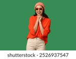 Cool African-American woman wearing hat and sunglasses on green background