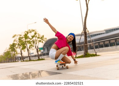 Cool Asian girl skating on longboard skate at park on summer holiday vacation. Stylish young woman having fun urban outdoor lifestyle practicing extreme sports skateboarding on city street at sunset. - Powered by Shutterstock