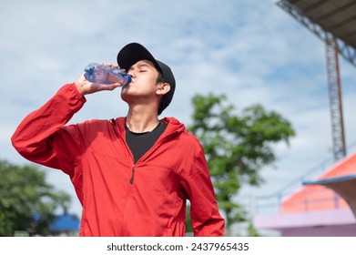 Cool Asian man in sportswear drinking water after exercising in the stadium Asian man drinking water after outdoor jogging at treadmill He exercises and carries a plastic water bottle. active living - Powered by Shutterstock