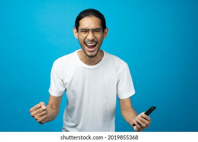 Cool Asian Woman Excited And Surprised By Smartphone On Blue Background. A Man Saw A Sale On An Online Shopping Website Or See The Results Of The Football Team Cheering Competition.