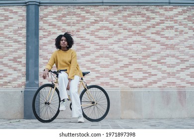 Cool black african american woman on a modern yellow fixie bike in front of pink brick wall
