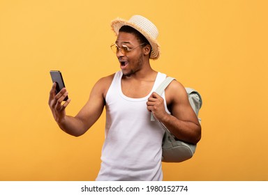 Cool black guy with backpack looking at his smartphone in excitement, booking last minute travel tour online, yellow studio background. African American man learning about big sale or discount - Powered by Shutterstock