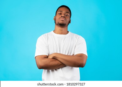 Cool Black Man Standing Crossing Hands Looking At Camera Posing On Blue Studio Background. Menacing Tough Guy's Portrait