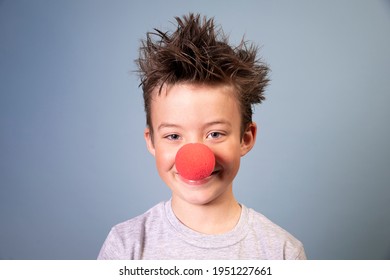 cool boy with wild hair posing with red clown nose on blue background and is happy