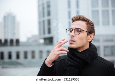 Cool Business man in glasses and warm clothes smoking cigarette on the street