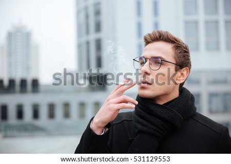 Cool Business man in glasses and warm clothes smoking cigarette on the street