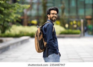 Cool cheerful young hindu guy wearing casual outfit with backpack walking by street, smiling at camera, going to job, copy space. Positive indian man student going to college, university - Powered by Shutterstock