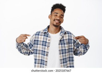 Cool and confident african american guy introduce logo, pointing fingers at center with smug pleased face, showing advertisement banner, standing against white background