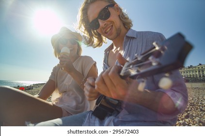 Cool Couple On A Beach Having Fun With A Musical Instrument And Ice Cream