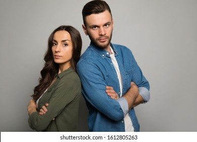 Cool Couple. Two Young People In Casual Outfits Are Standing Back To Back With Serious Facial Expressions, Posing With Folded Arms And Looking In The Camera.