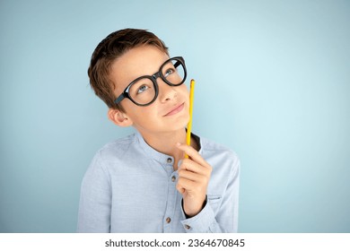 cool, cute young schoolboy with blue shirt, black glasses and pencil in front of blue background - Shutterstock ID 2364670845