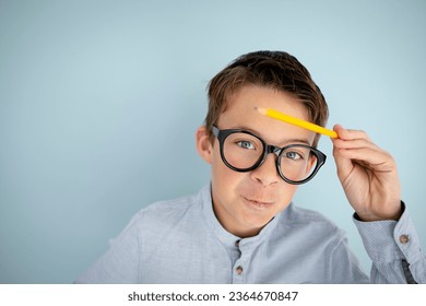 cool, cute young schoolboy with blue shirt, black glasses and pencil in front of blue background - Shutterstock ID 2364670847