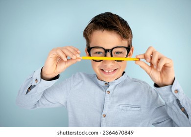 cool, cute young schoolboy with blue shirt, black glasses and pencil in front of blue background - Shutterstock ID 2364670849