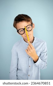 cool, cute young schoolboy with blue shirt, black glasses and pencil in front of blue background - Shutterstock ID 2364670851