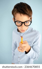 cool, cute young schoolboy with blue shirt, black glasses and pencil in front of blue background - Shutterstock ID 2364670855