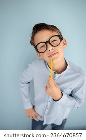 cool, cute young schoolboy with blue shirt, black glasses and pencil in front of blue background - Shutterstock ID 2364670857