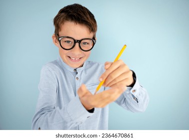cool, cute young schoolboy with blue shirt, black glasses and pencil in front of blue background - Shutterstock ID 2364670861