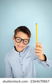 cool, cute young schoolboy with blue shirt, black glasses and pencil in front of blue background - Shutterstock ID 2364670867