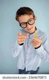 cool, cute young schoolboy with blue shirt, black glasses and pencil in front of blue background - Shutterstock ID 2364670871
