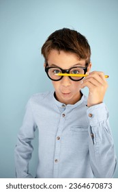 cool, cute young schoolboy with blue shirt, black glasses and pencil in front of blue background - Shutterstock ID 2364670873