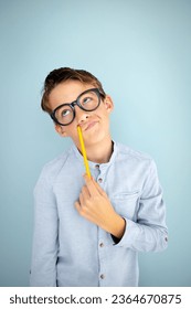 cool, cute young schoolboy with blue shirt, black glasses and pencil in front of blue background - Shutterstock ID 2364670875