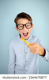 cool, cute young schoolboy with blue shirt, black glasses and pencil in front of blue background - Shutterstock ID 2364670877