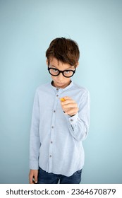 cool, cute young schoolboy with blue shirt, black glasses and pencil in front of blue background - Shutterstock ID 2364670879