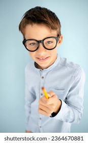 cool, cute young schoolboy with blue shirt, black glasses and pencil in front of blue background - Shutterstock ID 2364670881