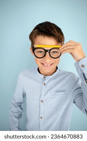 cool, cute young schoolboy with blue shirt, black glasses and pencil in front of blue background - Shutterstock ID 2364670883