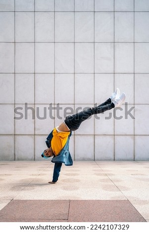 Cool dancer doing handstand in the street against white wall and looking at camera.